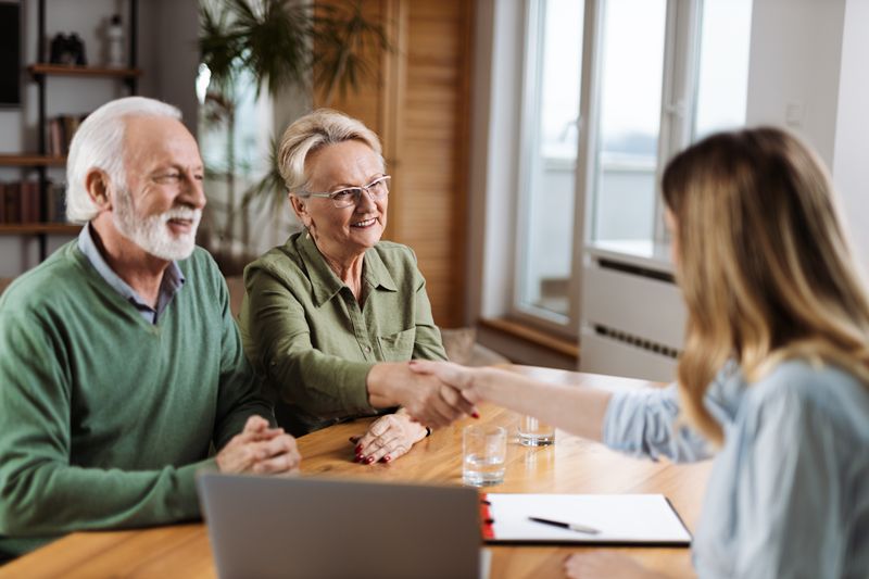 Happy senior woman shaking hands with a financial advisor after they came to an agreement at home