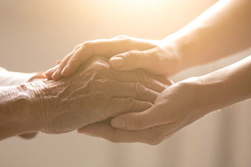 A Gentle Touch: A pair of hands, one aged and wrinkled, the other younger and smoother, clasped together in a gesture of comfort, compassion, and support, bathed in soft, warm light.